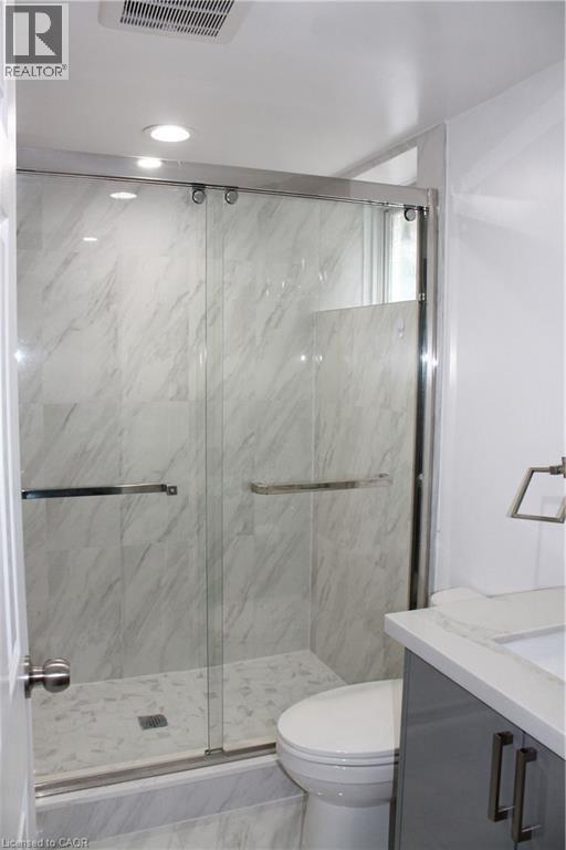 Shower enclosure with a clear glass sliding door, polished chrome hardware, and white marble-look tile - 27 Stillwater Street, Kitchener, ON