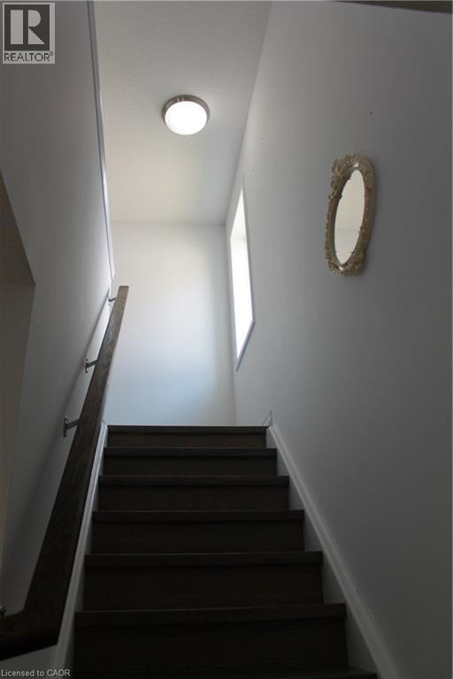 Stairwell with dark wood-finish treads and risers, a wood-finish handrail with brushed nickel supports, and a white ceiling-mounted light fixture - 27 Stillwater Street, Kitchener, ON