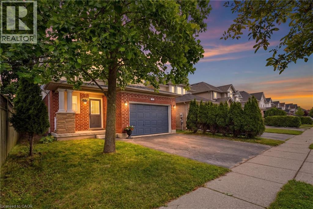 Brick facade residence featuring a front porch with stone columns, a dark blue garage door, and a paved driveway - 128 Houghton Street, Cambridge, ON