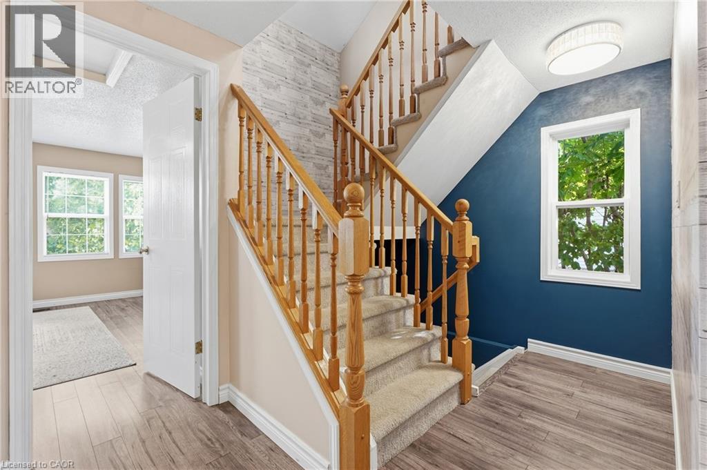 Two-story staircase with wood-finish balusters and newel posts, carpeted treads, and textured accent wall - 128 Houghton Street, Cambridge, ON