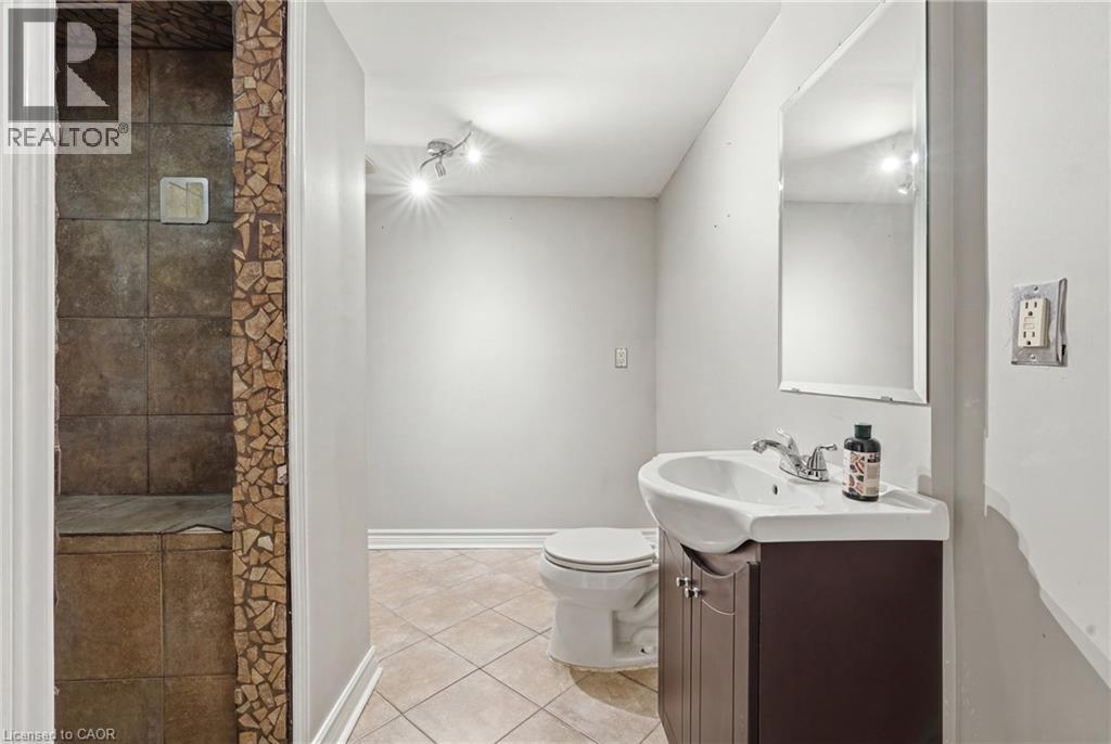Bathroom featuring an enclosed shower with stone-look tile, mosaic tile accents, a track light fixture, a toilet, and a vanity with an integrated sink and mirror - 128 Houghton Street, Cambridge, ON