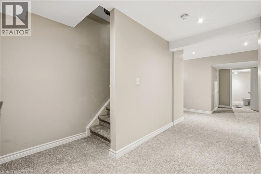 Recessed lighting illuminates a spacious carpeted area with neutral-toned walls and white baseboards - 128 Houghton Street, Cambridge, ON