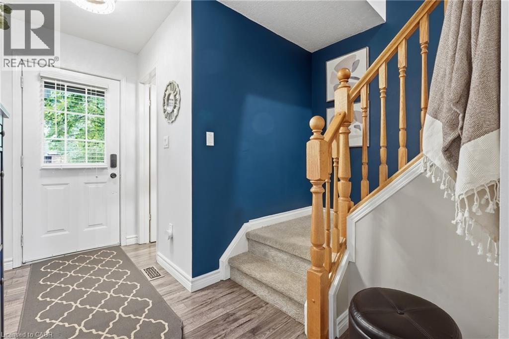 Entryway featuring a white door with an integrated window and horizontal blinds, wood-finish flooring, and a staircase with light wood banister and balusters - 128 Houghton Street, Cambridge, ON - Indoor Photo Showing Other Room