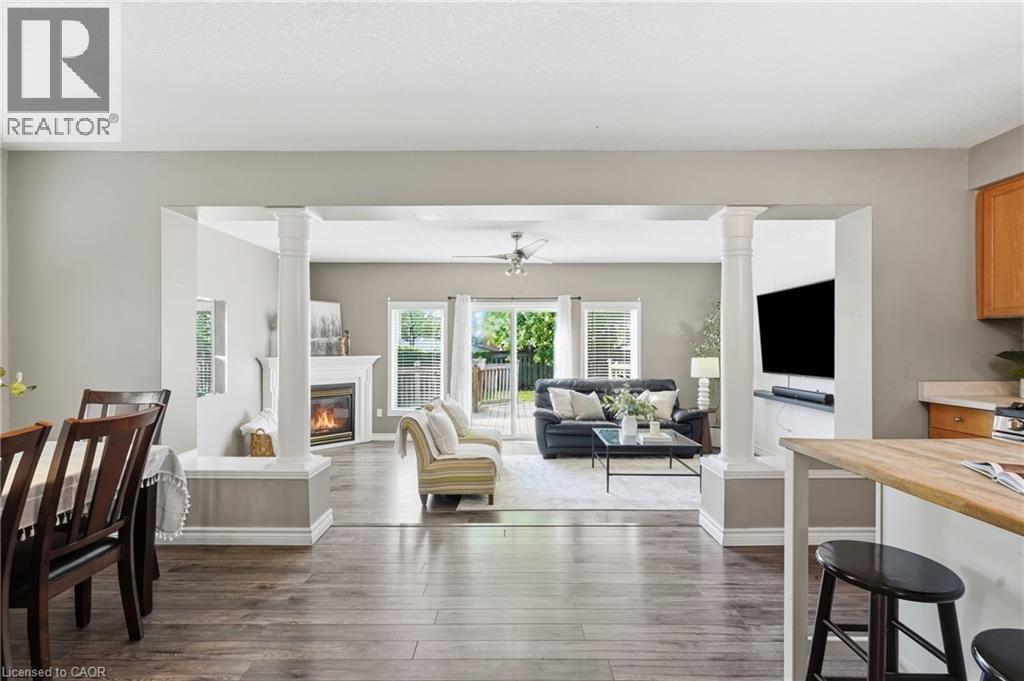 Open-concept living area with wood-finish flooring, a fireplace with white mantle, and a ceiling fan - 128 Houghton Street, Cambridge, ON
