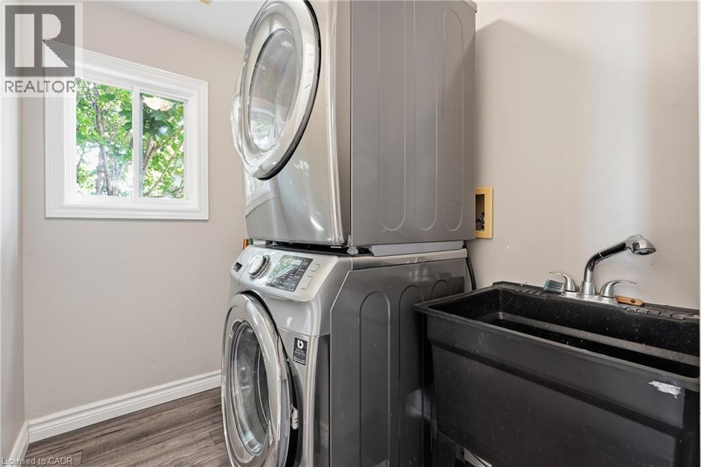 Dedicated laundry area featuring a stacked washer and dryer, a utility sink with a pull-out faucet, wood-finish flooring, and a window - 128 Houghton Street, Cambridge, ON - Indoor Photo Showing Laundry Room