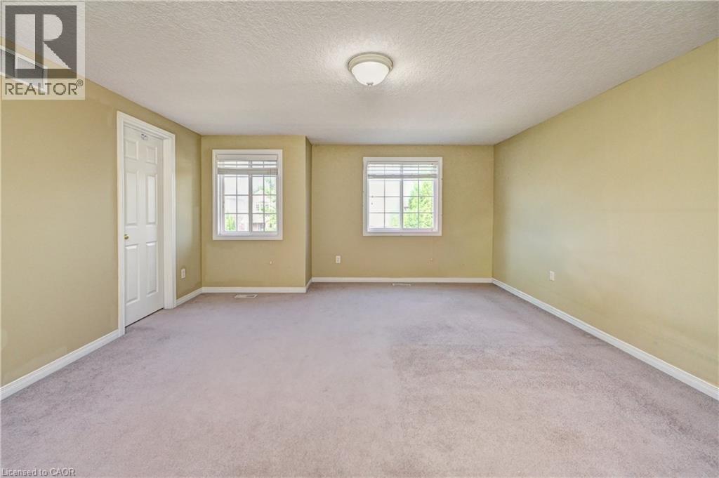 Spacious room featuring neutral carpeting, two windows with blinds, a white paneled door, and a flush-mount ceiling light - 760 Paris Boulevard, Waterloo, ON