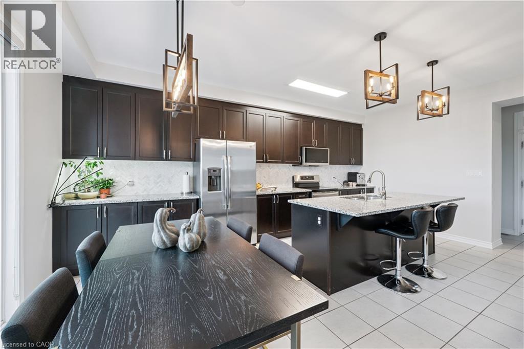 Kitchen featuring dark wood cabinetry, stainless steel appliances, a white tile backsplash, and a central island with bar seating - 87 Ridge Road, Cambridge, ON