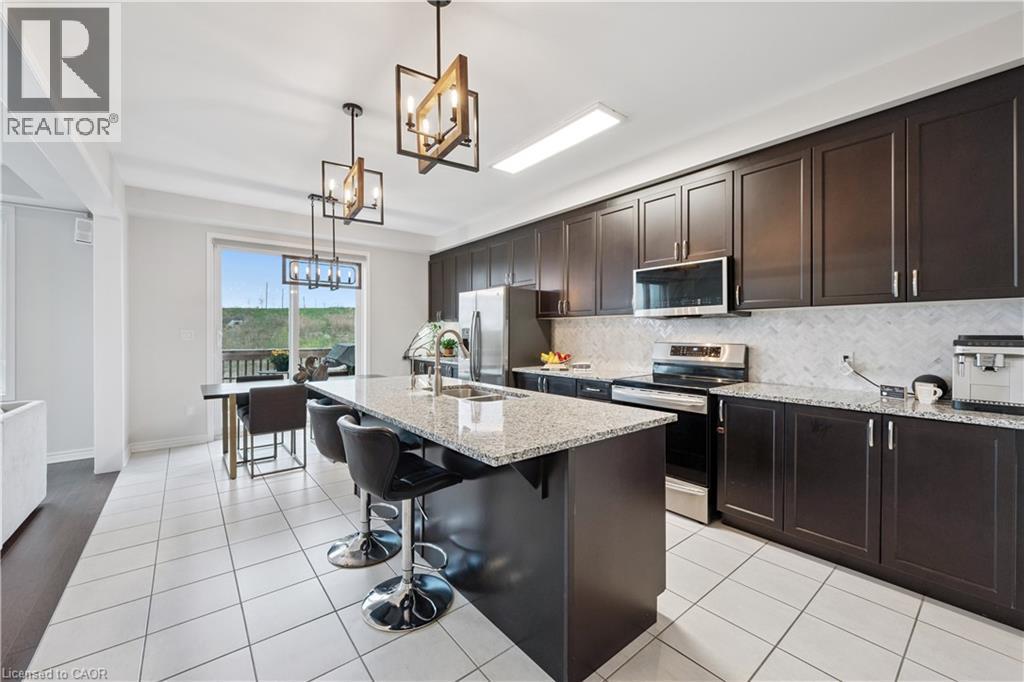 Well-appointed kitchen featuring dark wood cabinetry, stainless steel appliances, a center island with a stone countertop, and white tile flooring - 87 Ridge Road, Cambridge, ON