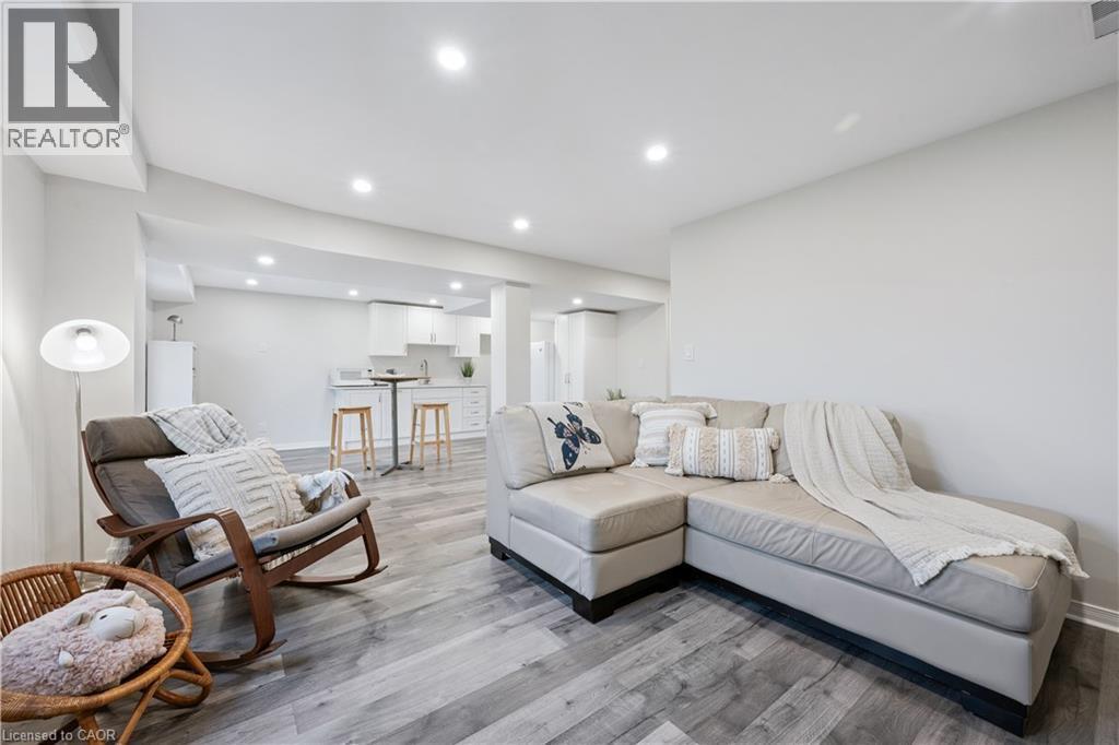 Open-concept room featuring light-toned wood-finish flooring, recessed lighting, white walls, and a visible kitchen area with white cabinetry - 87 Ridge Road, Cambridge, ON