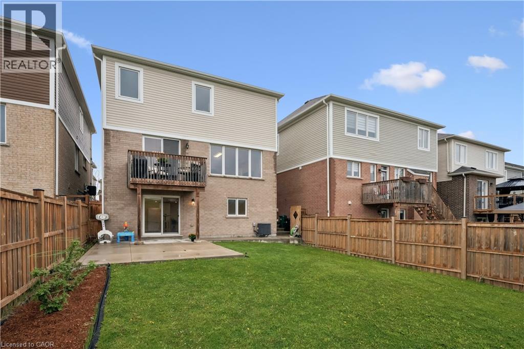 Expansive grassy backyard featuring a wooden fence, a concrete patio, and a second-story wooden balcony with railings - 87 Ridge Road, Cambridge, ON