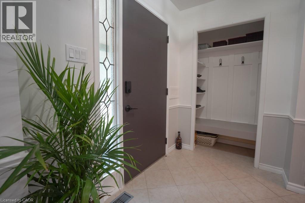 Entryway featuring a dark paneled door with decorative glass inserts, ceramic tile flooring, and a built-in mudroom area with shelving, hooks, and bench seating - 147 Muriel Crescent, London, ON