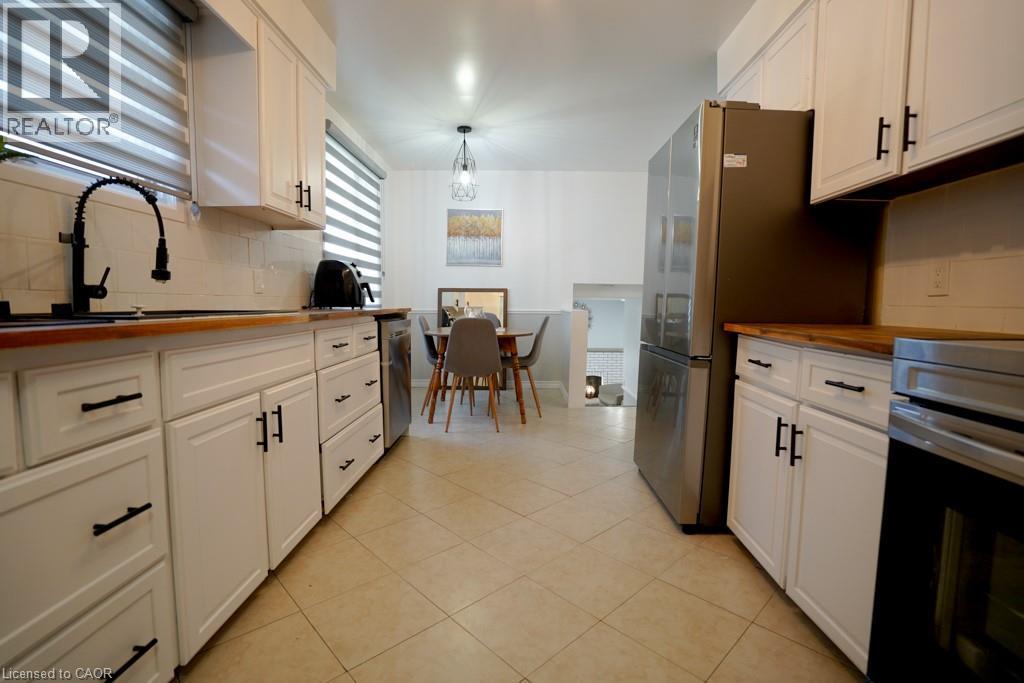 Kitchen featuring white shaker-style cabinetry, dark hardware, wood-finish countertops, stainless steel appliances, and tile flooring - 147 Muriel Crescent, London, ON