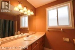 Bathroom featuring a single vanity with an integrated sink, a large mirror, a multi-light fixture, and a window with frosted glass - 17 Hawkswood Drive, Kitchener, ON