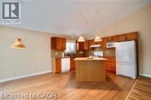 Vaulted ceilings accent this kitchen featuring wood-finish flooring, wood cabinetry, a central island, and white appliances - 17 Hawkswood Drive, Kitchener, ON