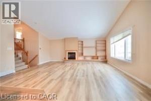 Spacious interior featuring wood-finish flooring, a built-in fireplace with mantle, integrated shelving, and a large window - 17 Hawkswood Drive, Kitchener, ON