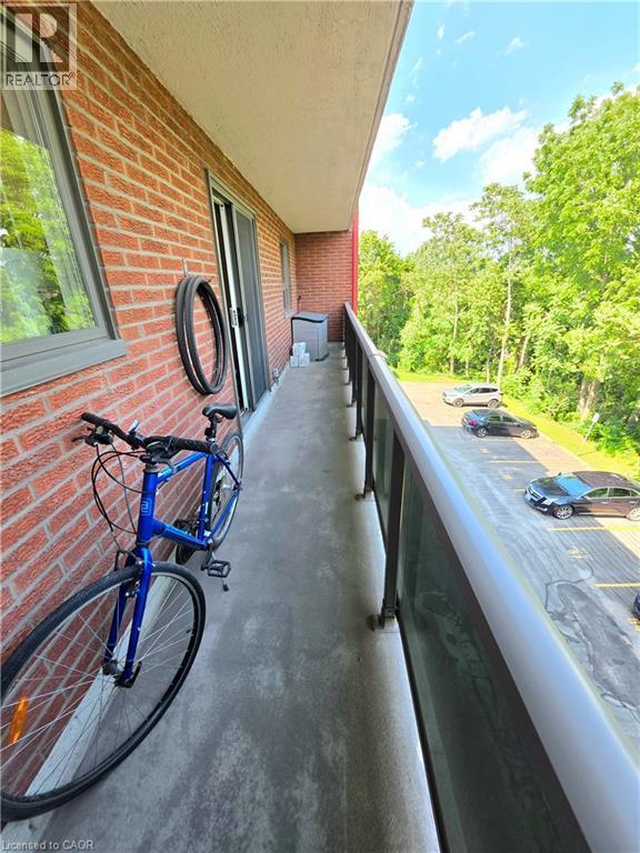 Outdoor balcony featuring a concrete floor, red brick exterior, sliding glass door, and metal railing with opaque panels - 2373 E King Street E Unit# 37, Hamilton, ON
