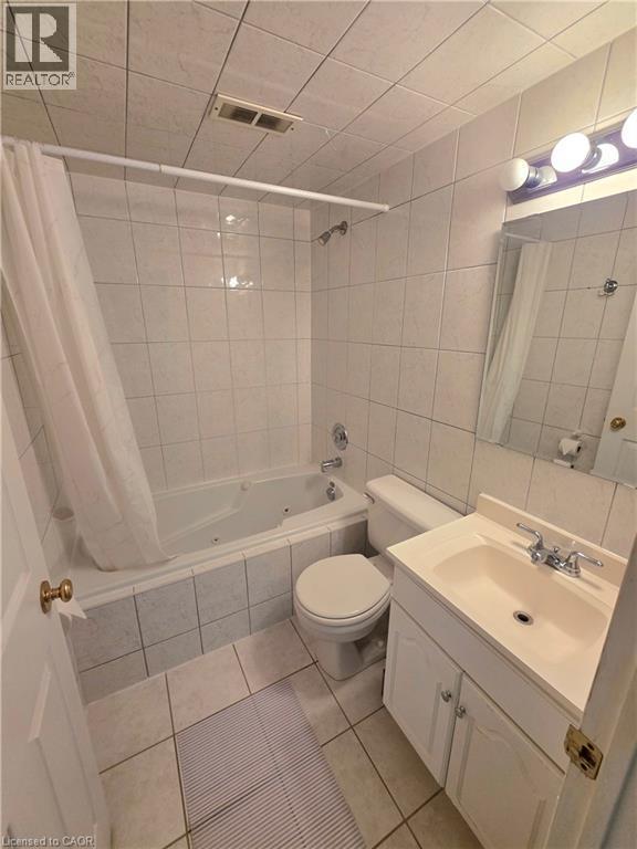 Bathroom featuring a jetted tub, ceramic tile surround and flooring, white vanity with integrated sink, and chrome fixtures - 2373 E King Street E Unit# 37, Hamilton, ON