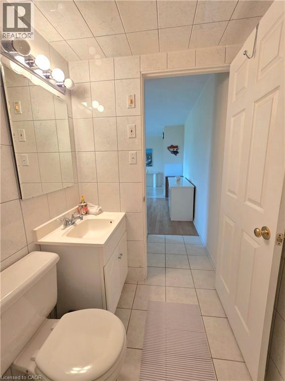 Bathroom featuring floor-to-ceiling white tile, a white vanity with integrated sink, a mirrored wall cabinet, and a chrome light fixture - 2373 E King Street E Unit# 37, Hamilton, ON