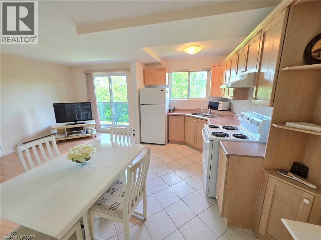 Open-concept living space featuring a kitchen with wood-finish cabinetry, white appliances, and a tiled floor - 2373 E King Street E Unit# 37, Hamilton, ON