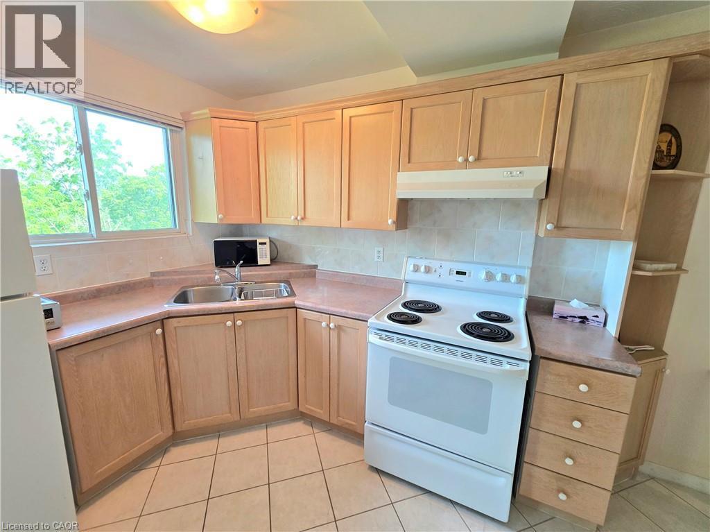 Kitchen featuring wood-finish cabinetry, a double basin stainless steel sink, and a white electric range with an overhead vent - 2373 E King Street E Unit# 37, Hamilton, ON