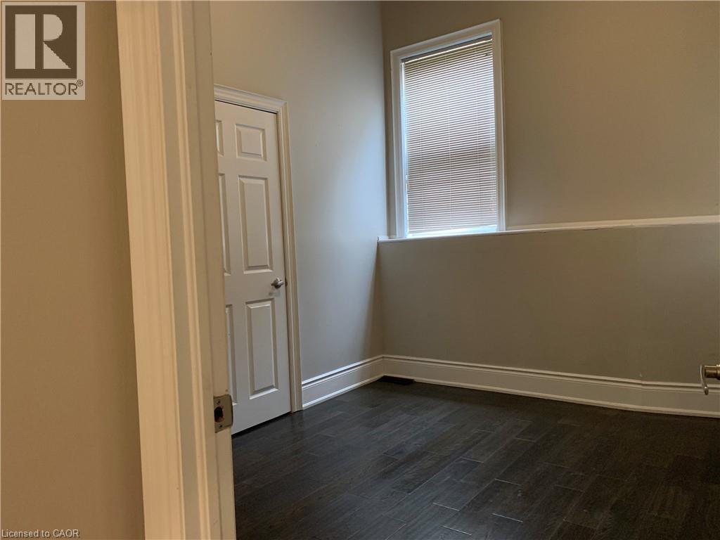 Unit 2 bedroom featuring dark wood-finish flooring, neutral wall paint, and white trim - 405 Macnab Street N, Hamilton, ON