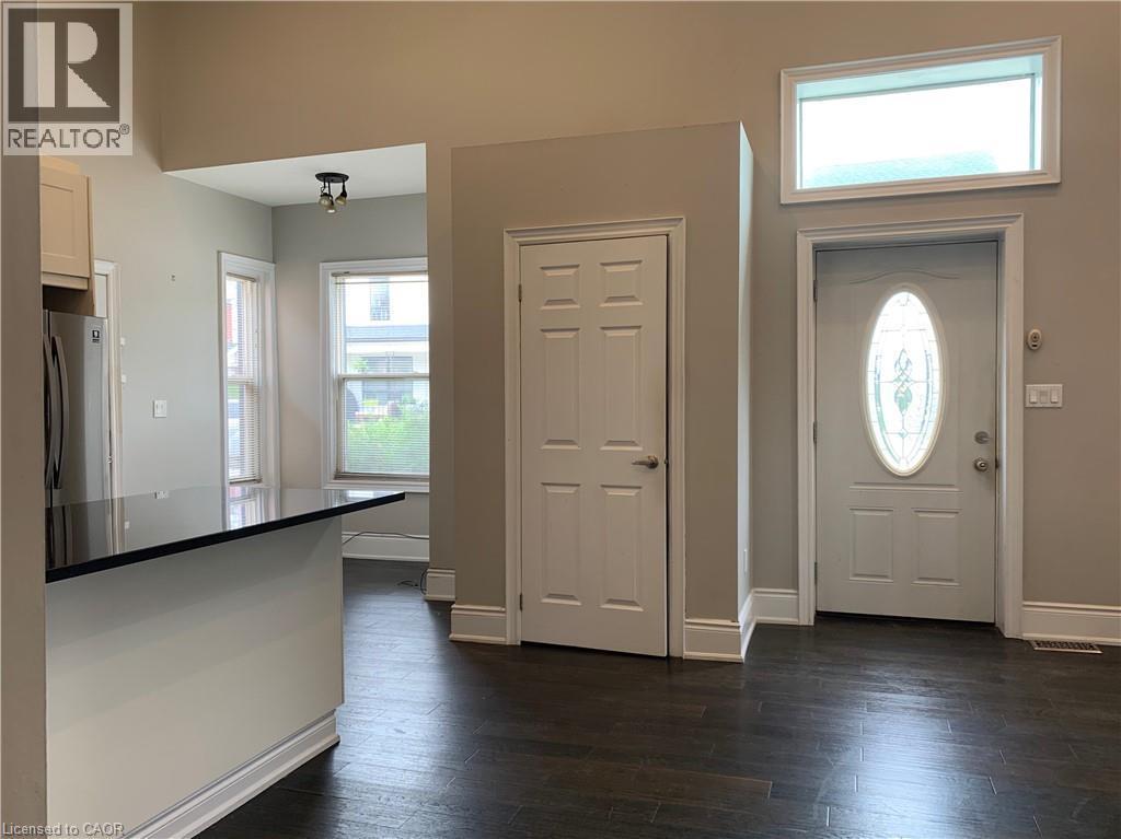 Unit 1 Open-concept living space featuring dark wood-finish flooring, a contemporary kitchen island with a dark countertop, and a white entry door with an oval-shaped decorative glass insert - 405 Macnab Street N, Hamilton, ON