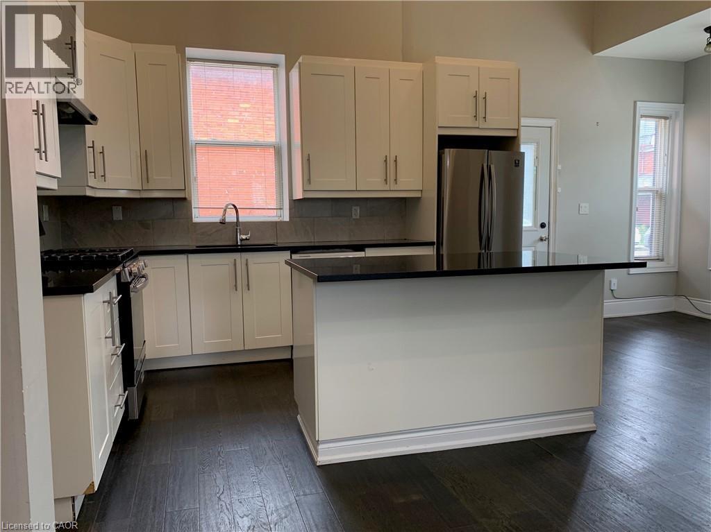 Unit 1 kitchen featuring white shaker cabinetry, dark countertops, stainless steel appliances, a center island, and wood-finish flooring - 405 Macnab Street N, Hamilton, ON
