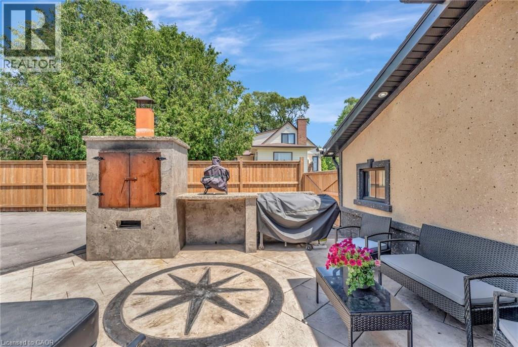 Expansive outdoor patio featuring an integrated stone oven with a terracotta chimney, a concrete prep counter, and a decorative compass rose inlay - 192 Myers Road, Cambridge, ON