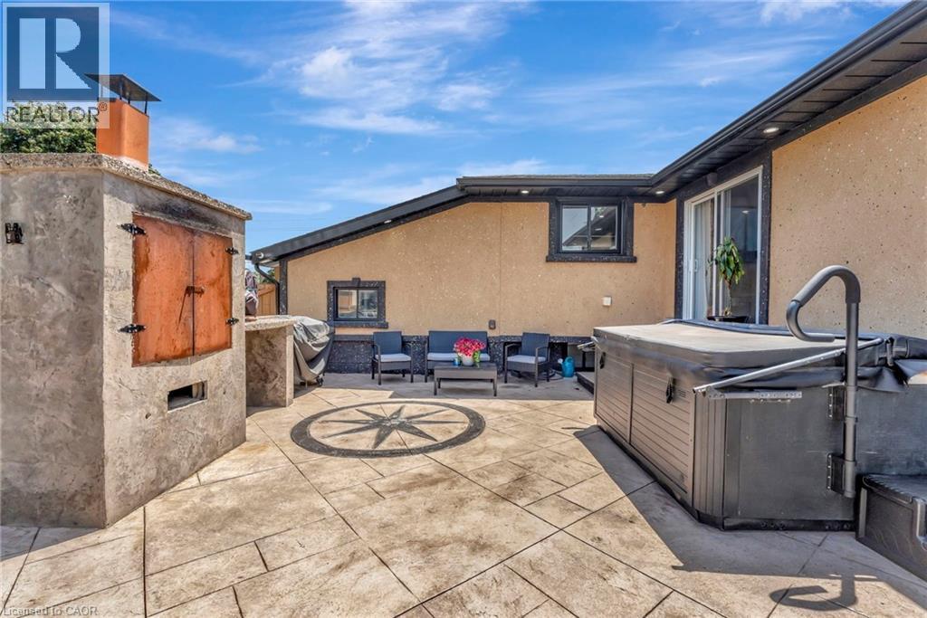 Stamped concrete patio featuring an outdoor cooking structure with a chimney, a built-in hot tub, a compass rose inlay, and a sliding glass door entry to the building - 192 Myers Road, Cambridge, ON