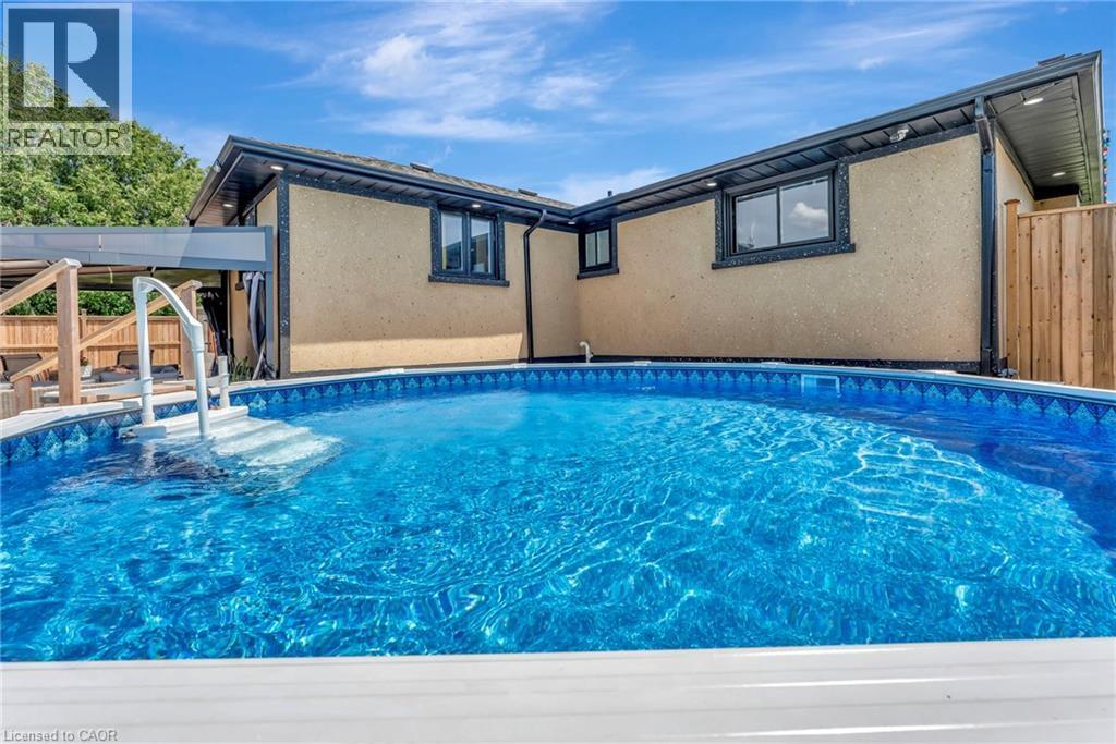 In-ground pool with integrated steps, surrounded by a light-toned exterior finish and dark-framed windows - 192 Myers Road, Cambridge, ON