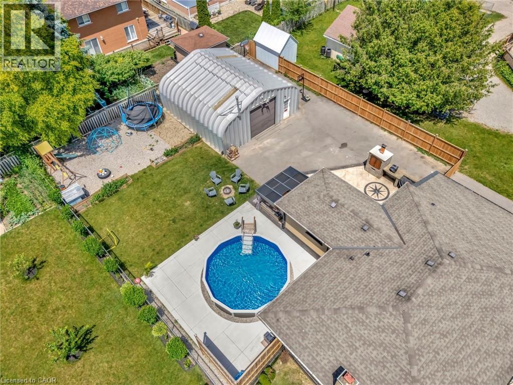 Expansive backyard featuring an above-ground swimming pool with concrete surround, an outdoor kitchen with built-in grill and chimney, a large detached quonset hut, and a separate gravel area - 192 Myers Road, Cambridge, ON