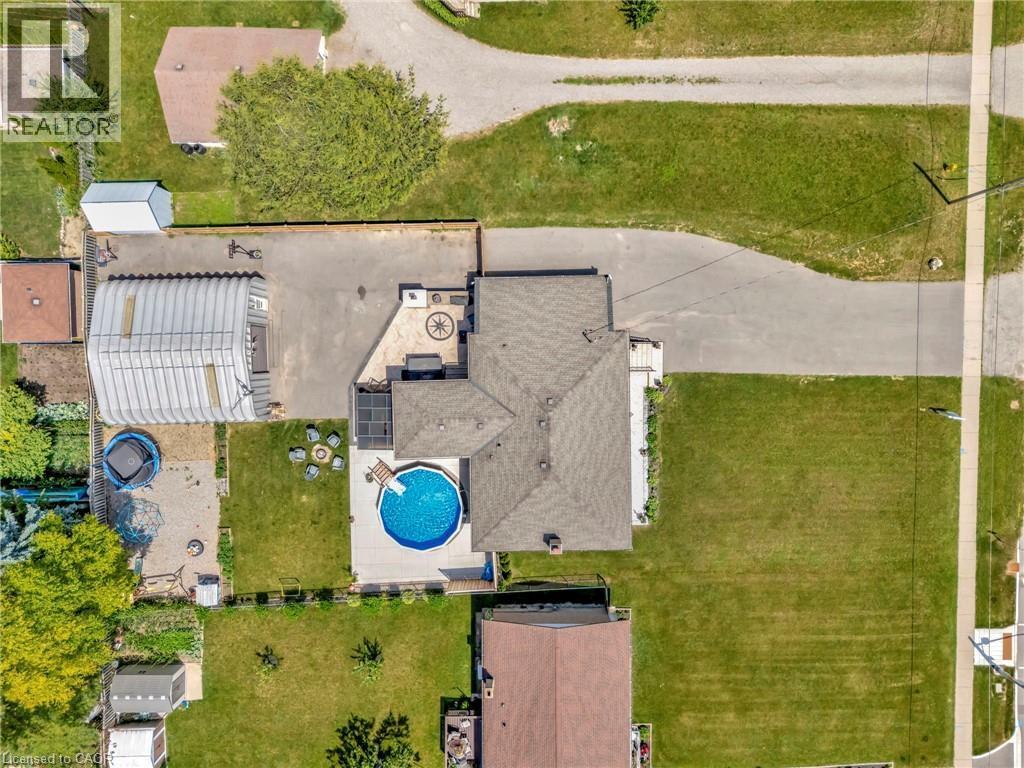 Expansive property featuring a circular above-ground pool, a paved patio with an inset decorative compass design, a large paved driveway, a detached metal structure, and a secondary paved area - 192 Myers Road, Cambridge, ON