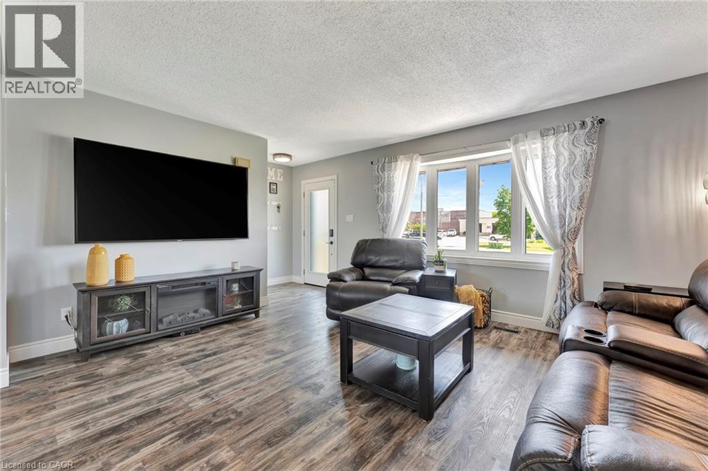 Spacious living area featuring wood-finish flooring, light gray walls, a large multi-pane window, and a built-in media console with glass-front cabinets - 192 Myers Road, Cambridge, ON