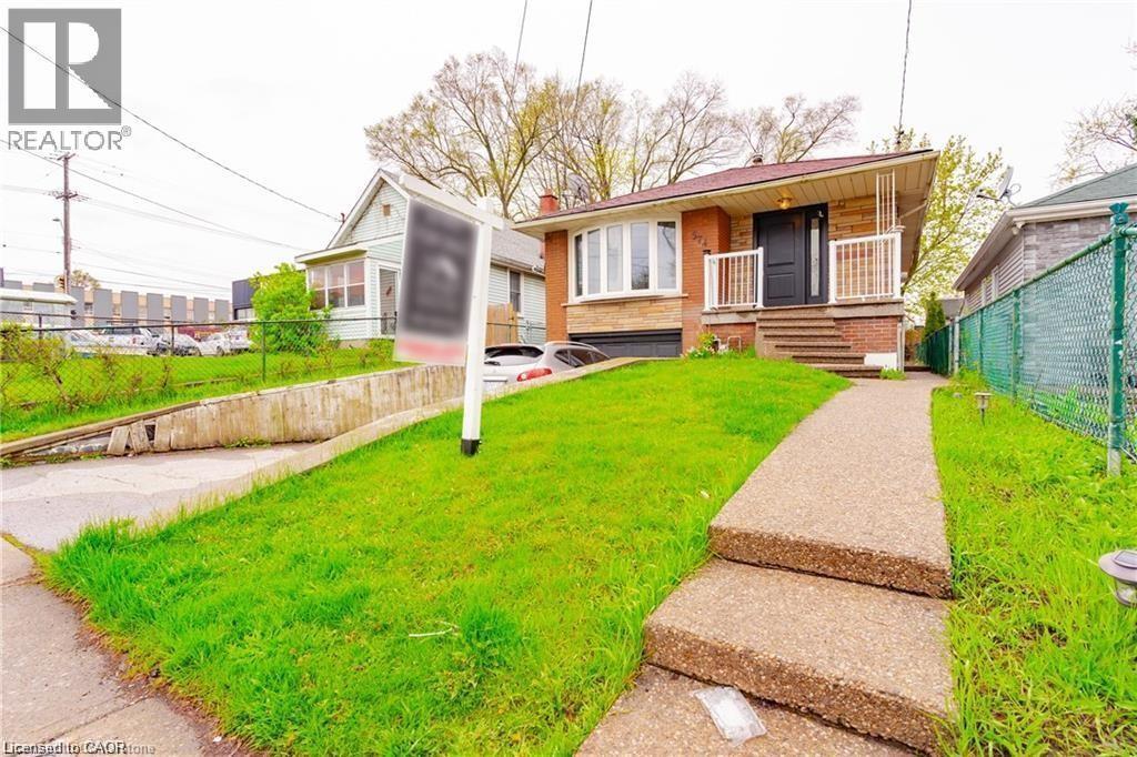 Brick exterior featuring a bay window, concrete front walk with steps, a covered porch with white railings, and a driveway leading to an integrated garage - 574 Upper Sherman Avenue, Hamilton, ON