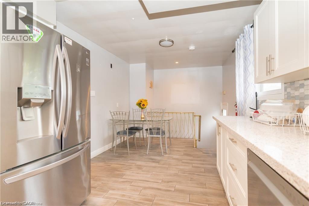 Kitchen featuring wood-finish tile flooring, white shaker cabinetry with brushed nickel hardware, a light-toned countertop, a mosaic tile backsplash, and a stainless steel refrigerator - 574 Upper Sherman Avenue, Hamilton, ON