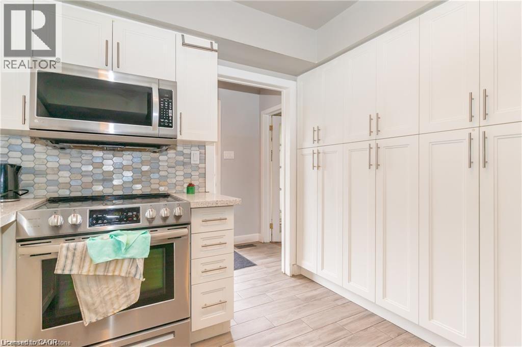 Modern kitchen featuring white shaker cabinetry with brushed nickel hardware, stainless steel appliances, a mosaic tile backsplash, and wood-finish flooring - 574 Upper Sherman Avenue, Hamilton, ON