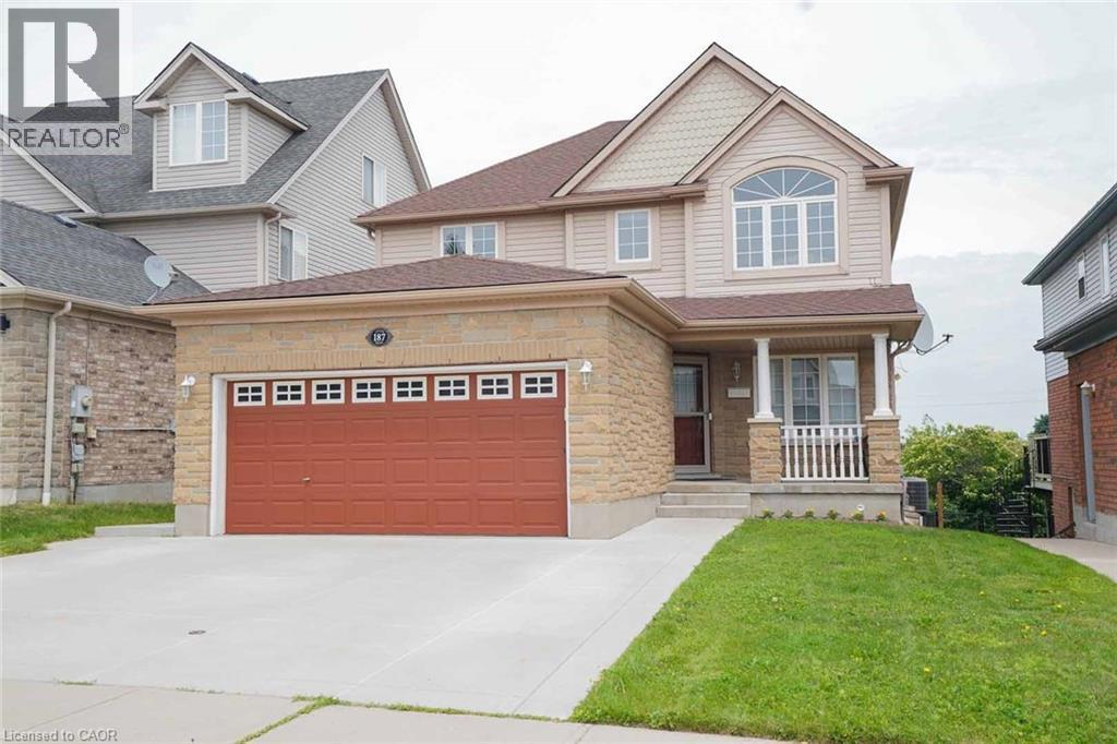 Two-story residence featuring a brick and siding facade, an arched window, a covered front porch with white railings, a two-car garage with a red door, and an asphalt shingle roof - 187 Adler Drive, Cambridge, ON - Outdoor With Facade