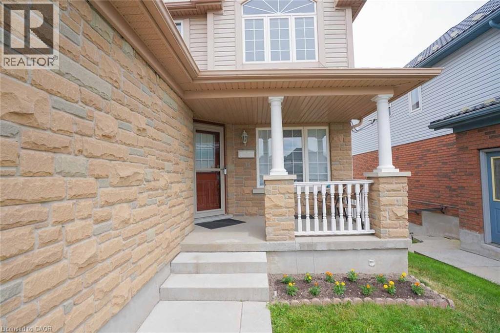 Stone facade residence featuring a covered front porch with decorative columns and railings, a main entry door with a screen door, concrete steps, and an upper-level bay window - 187 Adler Drive, Cambridge, ON - Outdoor