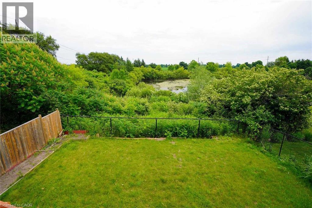 Expansive green lawn area featuring a wooden privacy fence, black chain-link fencing, and a natural wetland area with mature trees and foliage - 187 Adler Drive, Cambridge, ON - Outdoor