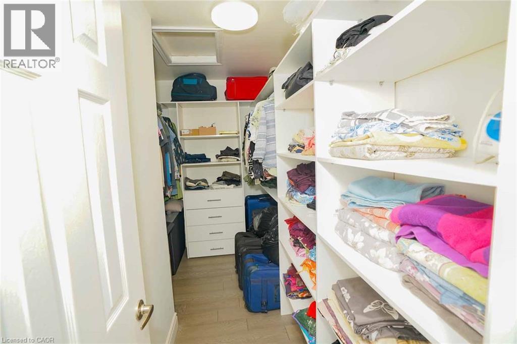 Walk-in closet featuring built-in white shelving, integrated drawers, hanging rods, recessed lighting, and wood-finish flooring - 187 Adler Drive, Cambridge, ON - Indoor
