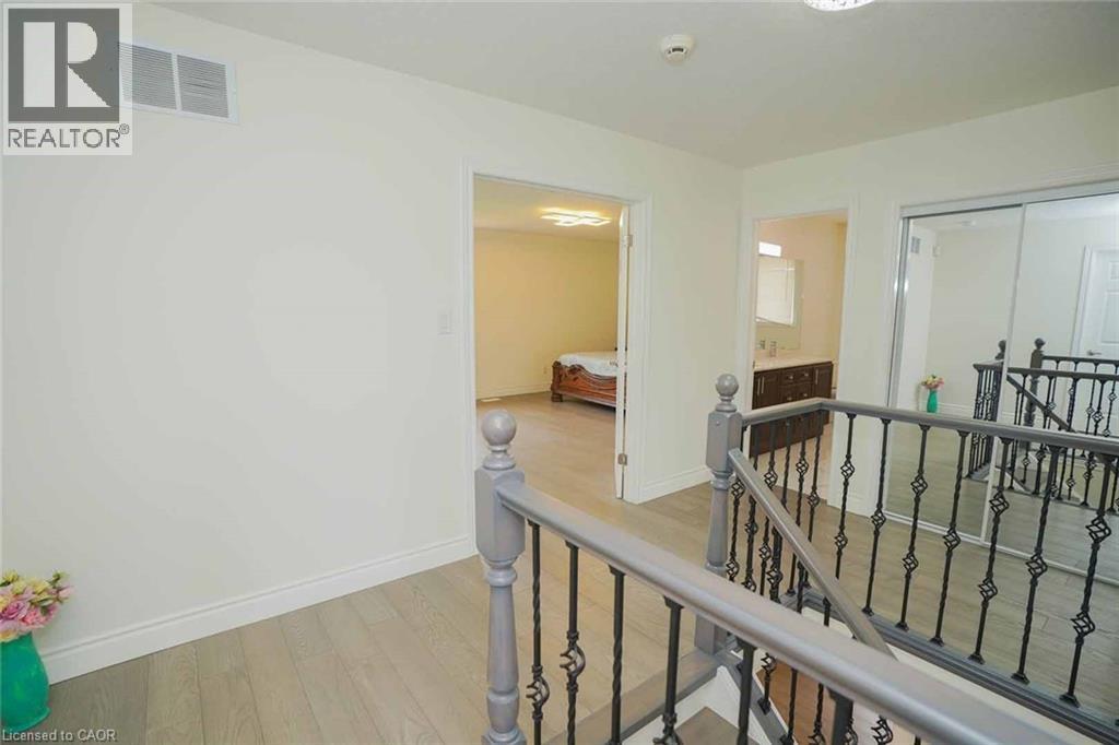 Upper hallway featuring light wood-finish flooring, wrought iron railings, and a built-in mirrored closet - 187 Adler Drive, Cambridge, ON - Indoor Photo Showing Other Room
