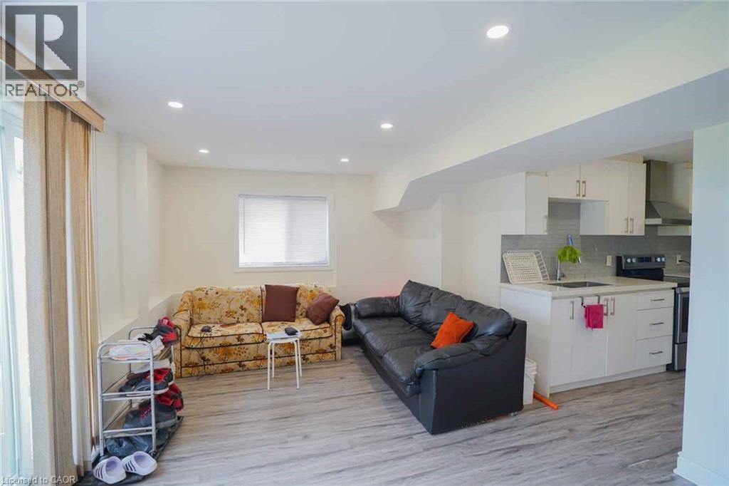Open-concept living space featuring wood-finish flooring, recessed lighting, and a modern kitchen with white cabinetry, stainless steel appliances, and a tiled backsplash - 187 Adler Drive, Cambridge, ON - Indoor