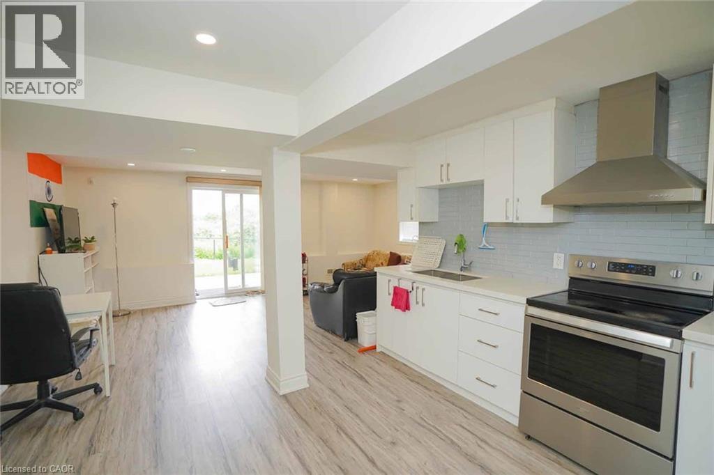 Modern kitchen featuring white cabinetry, stainless steel appliances, a light-toned countertop, and a tiled backsplash, opening to a spacious area with wood-finish flooring and sliding glass doors - 187 Adler Drive, Cambridge, ON - Indoor Photo Showing Kitchen