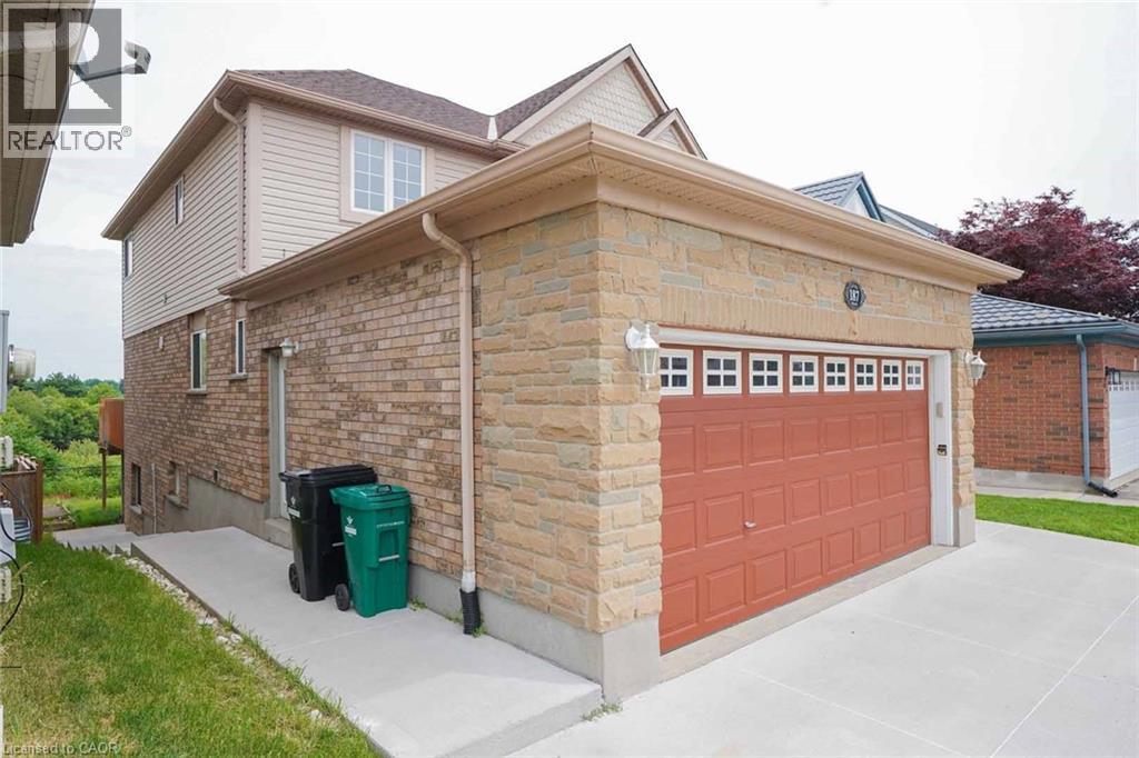 Stone and siding exterior with an attached garage, featuring a panel-style garage door with decorative window inserts, and sconce lighting - 187 Adler Drive, Cambridge, ON - Outdoor With Exterior