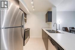 Modern kitchen featuring stainless steel appliances, track lighting, light-toned flooring, dark wood-finish cabinetry, and solid surface countertops with an undermount dual-basin sink - 
