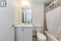 Bathroom featuring a white vanity with integrated sink and chrome faucet, a white toilet, and a bathtub with tiled surround - 