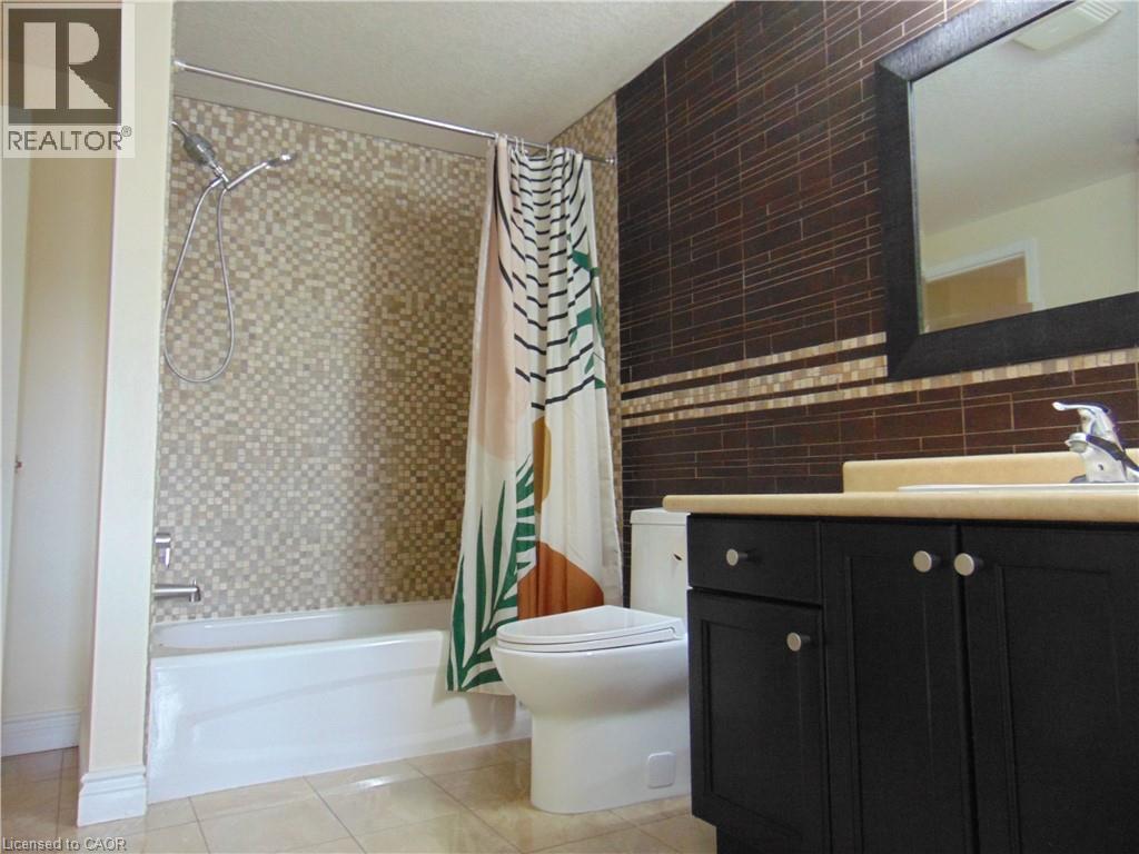Bathroom featuring a white tub, mosaic tile surround, dark wood-finish vanity with a light countertop, and a framed mirror - 214 Snowdrop Crescent, Kitchener, ON