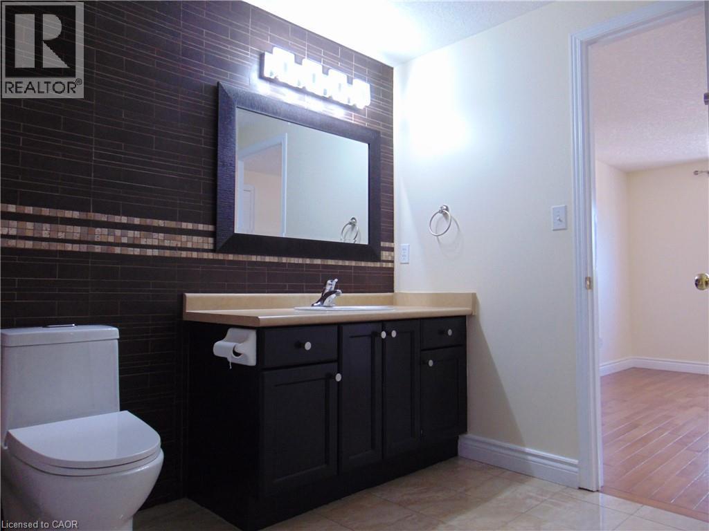 Bathroom featuring a dark tiled accent wall with a mosaic band, a black vanity with a light countertop, a framed mirror, and a modern toilet - 214 Snowdrop Crescent, Kitchener, ON