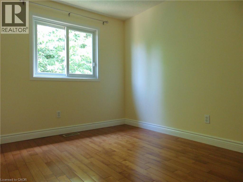 Warm-toned walls complement wood-finish flooring in this room featuring a sliding window - 214 Snowdrop Crescent, Kitchener, ON