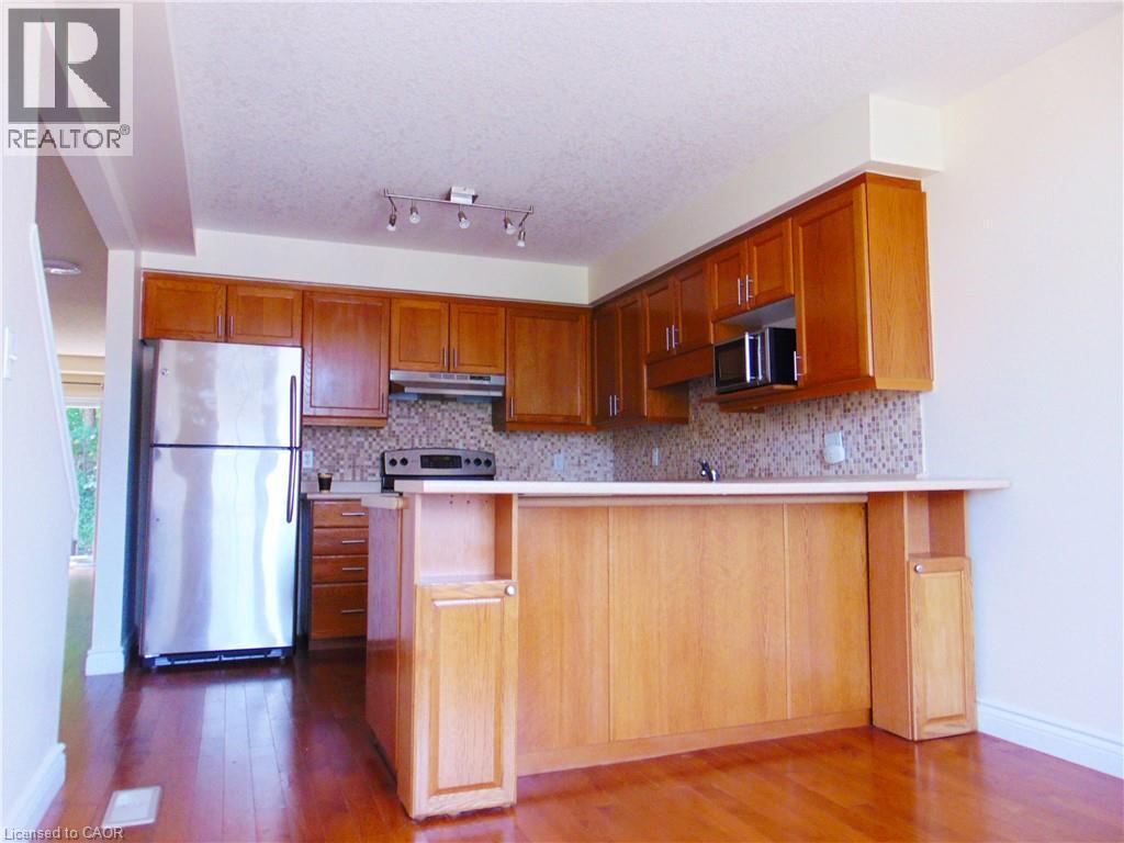 Kitchen featuring wood-finish flooring, stainless steel appliances, a breakfast bar, and a mosaic tile backsplash - 214 Snowdrop Crescent, Kitchener, ON - Indoor Photo Showing Kitchen